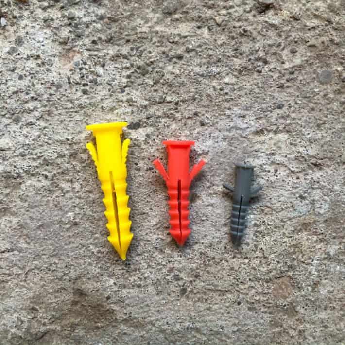 A yellow, red and grey plastic wall anchor with wings pulled out.