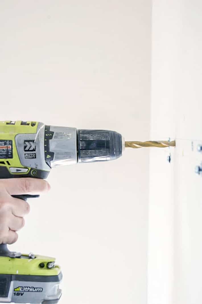 Bright green Ryobi drill, drilling into white wall.