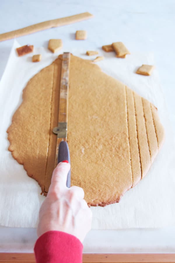 Cutting baked gingerbread dough with a pizza wheel into 1" wide strips.
