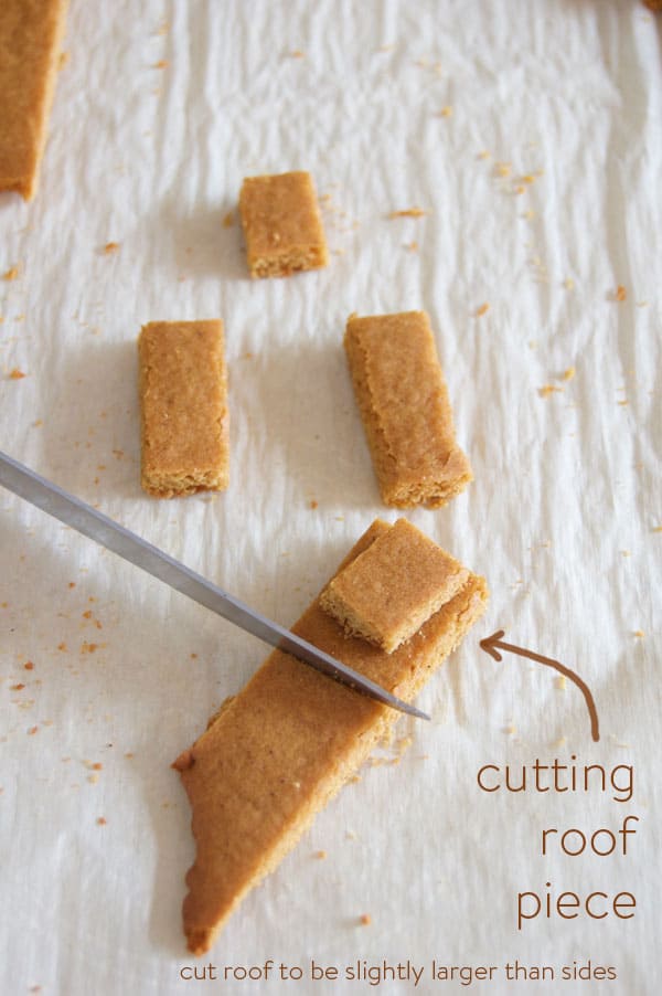 Cutting a piece of gingerbread roof with a paring knife on parchment paper.