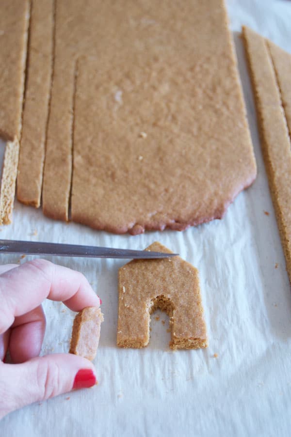 Cutting tiny house front out of a sheet of baked gingerbread.