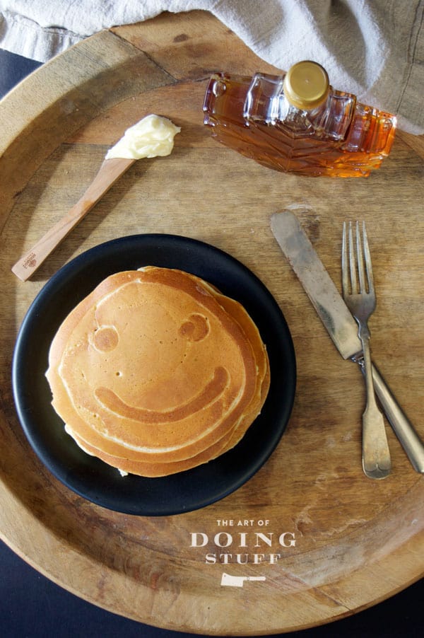 Smiley face pancake on wood tray.