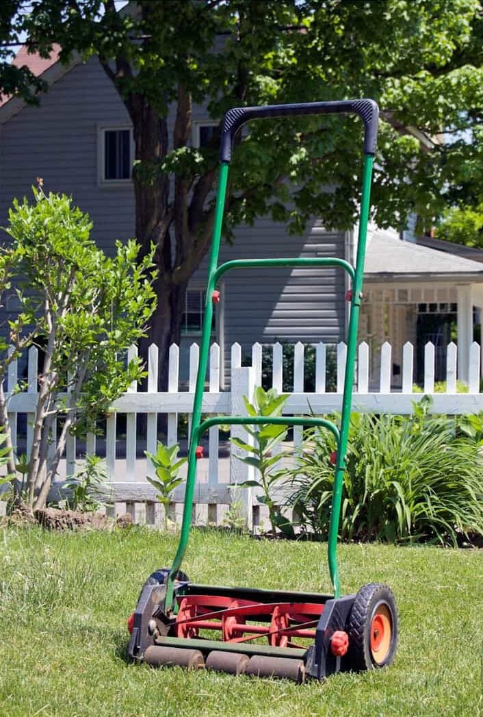 Push mower standing on lawn with white picket fence in background