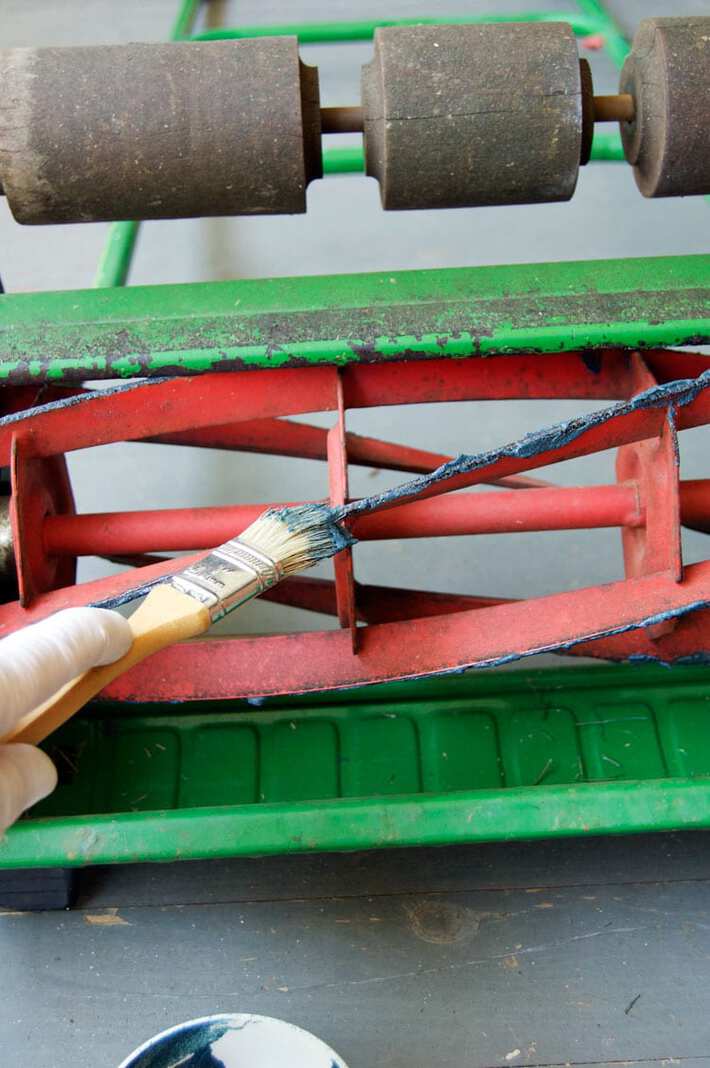 Applying sharpening compound to the red blades of a push mower with a brush.
