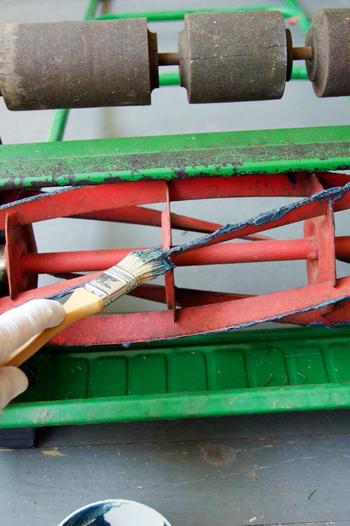 How to sharpen your push mower's blades. Applying sharpening compound to the red blades of a push mower with a brush.