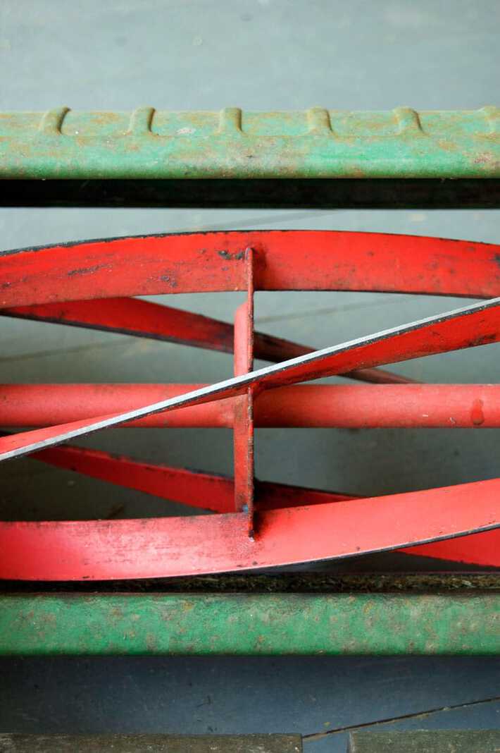 How to sharpen your push mower's blades. Close up view of silvery blades on the red reel of a push mower, newly sharpened.