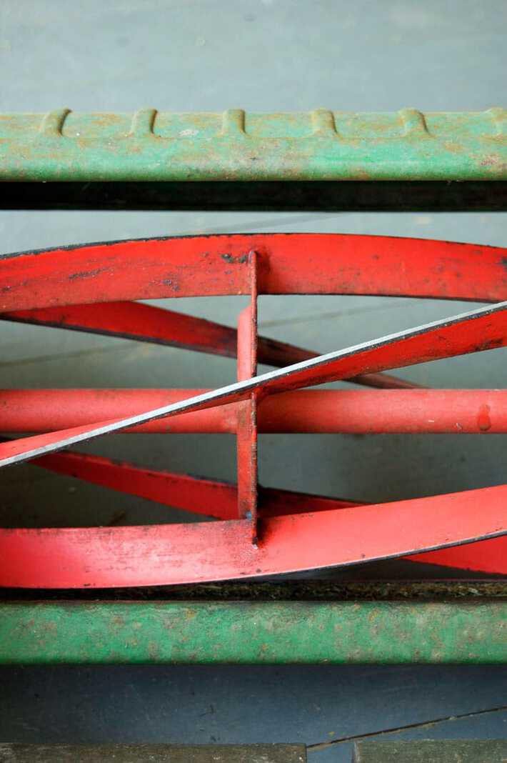 Close up view of silvery blades on the red reel of a push mower, newly sharpened.