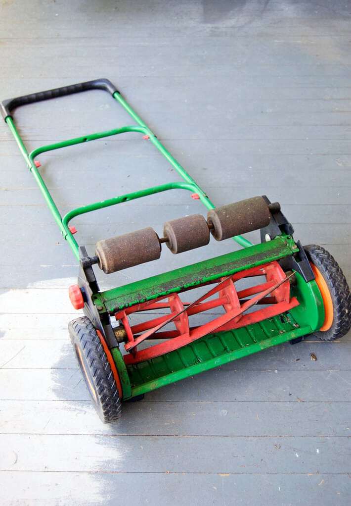 Green and red push mower laying down on grey painted porch.