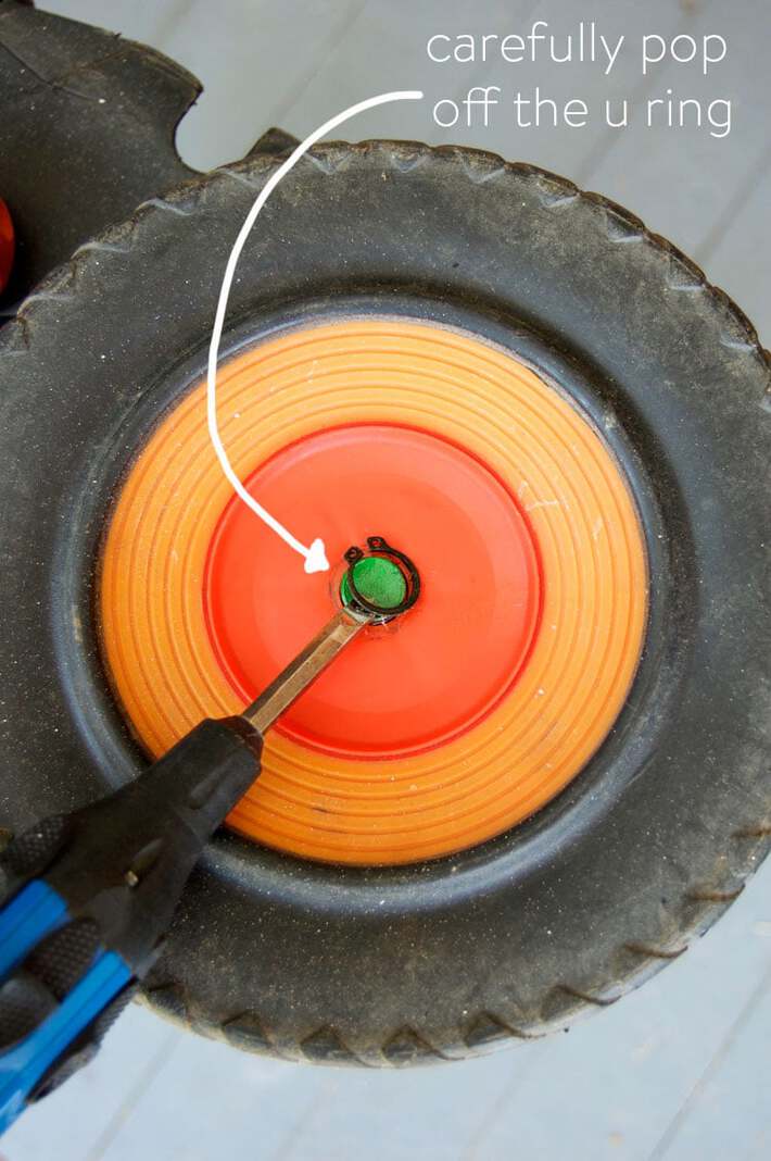 Using a flathead screwdriver to pry off a u ring on a push mower wheel.