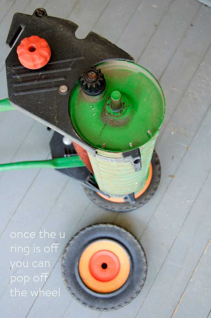 Wheel removed and laying on ground beside a push mower ready to have the blades sharpened with compound.