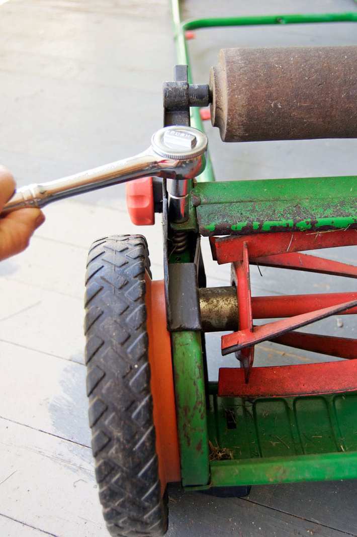 Moving the cutting bar closer to the reel blades on a push mower using a ratchet. 