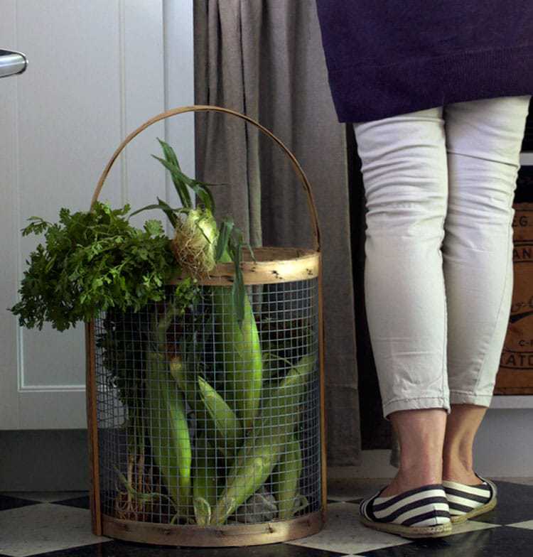 Wire basket with wood trim and handles filled with garden produce like carrots and corn.