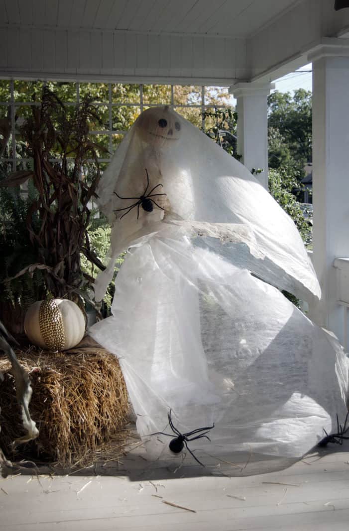 Ghost bride made with foam pumpkin, a fan and garden netting blows in the wind on a front porch.