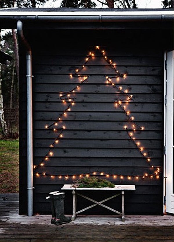 The shape of a Christmas tree is outlined with lights on the side of a black shed.