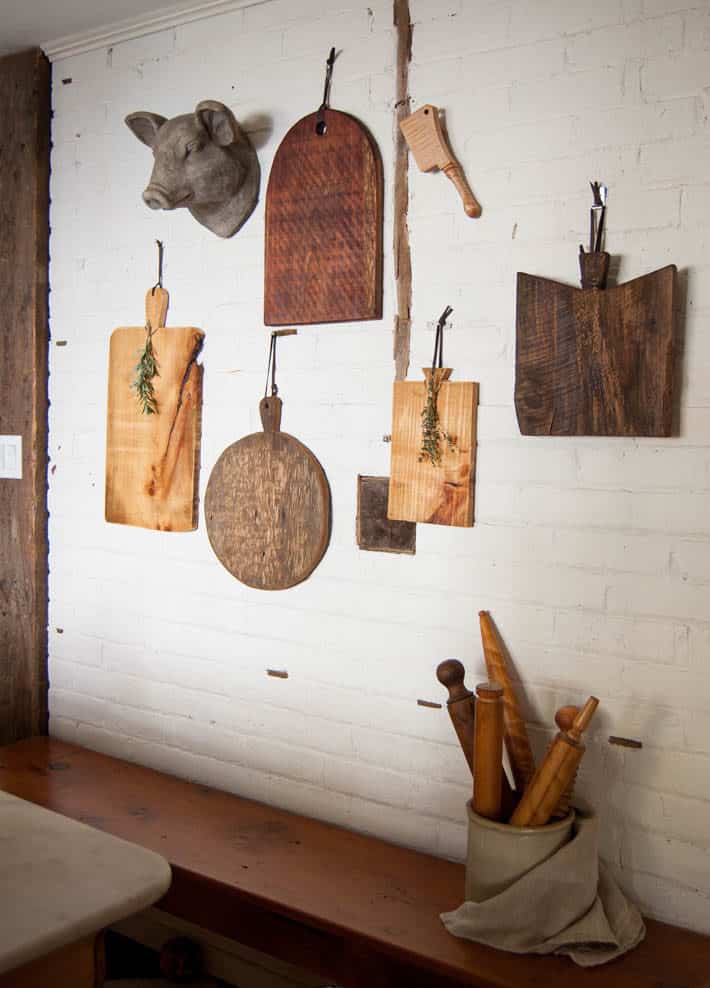 Make your own "antique" wood serving board in about 2 hours. 5 wood DIY meat and cheese platters hanging on a white painted brick wall.