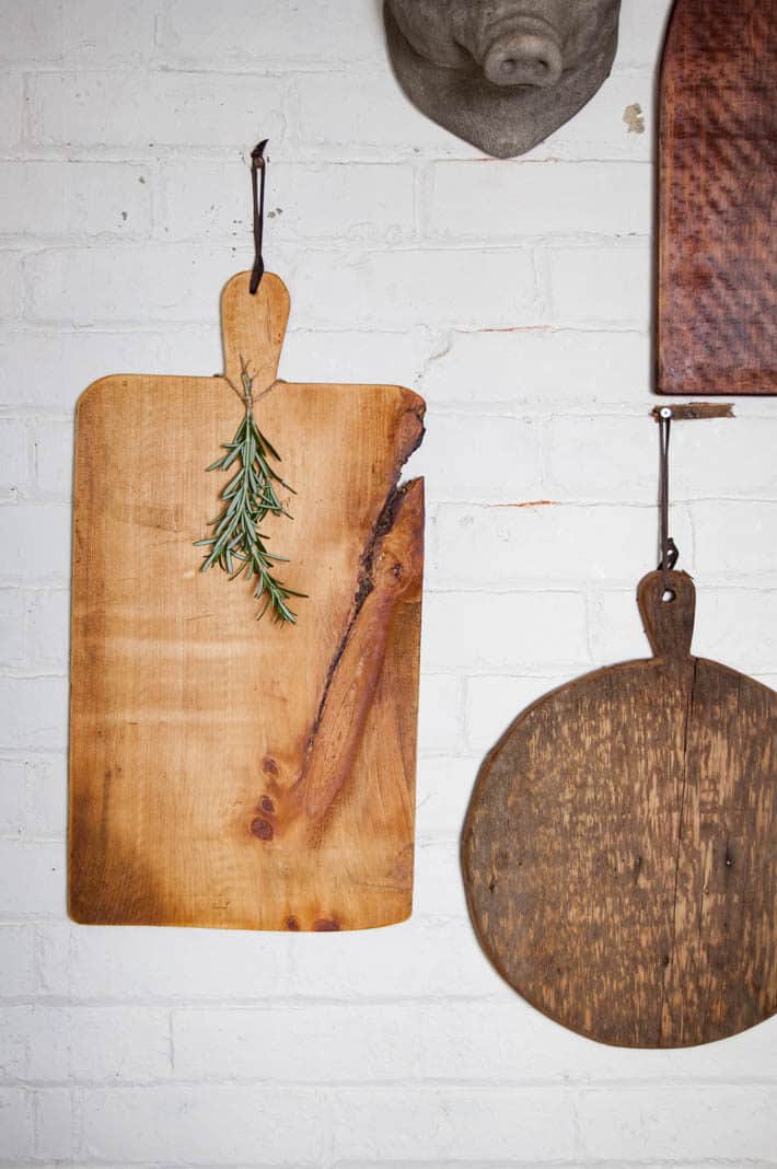 Glowing pine DIY serving board hanging on a brick wall by a leather tie.