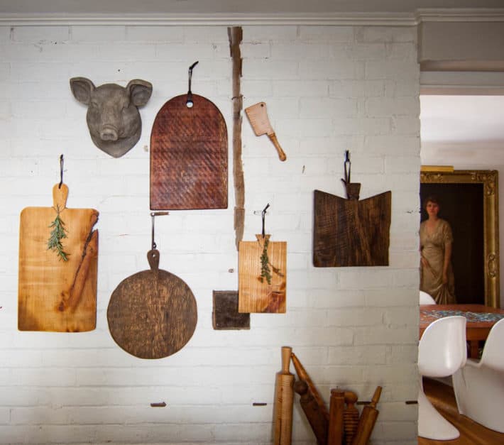 Make your own "antique" wood serving board in about 2 hours. Various shapes and sizes of DIY charcuterie boards hanging on white brick wall.