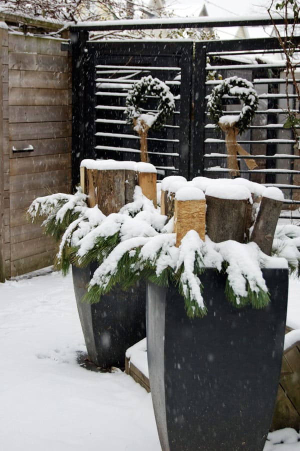 Christmas planters with evergreen branches surrounding small stacks of wood in each.