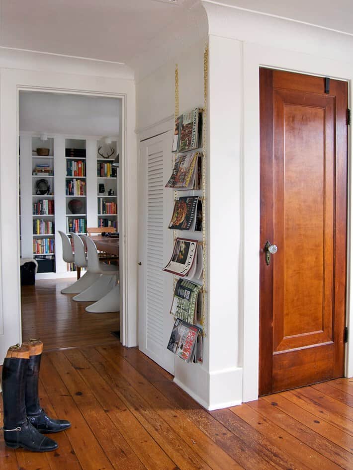 White room with wood floors, gold chain magazine rack hanging on wall.