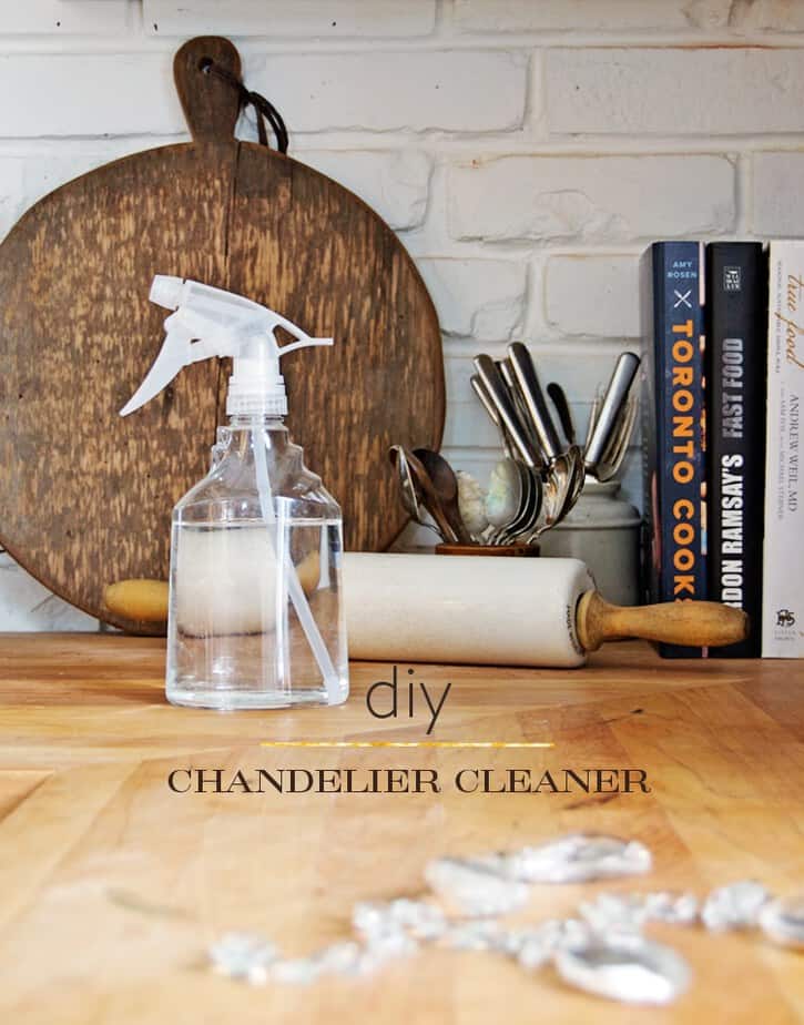 DIY chandelier cleaner in a spray bottle on a wood countertop with white brick walls.