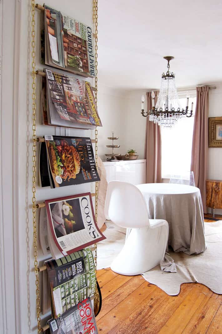 Floor to ceiling hanging magazine rack with gold chain sides and natural dowel bars.