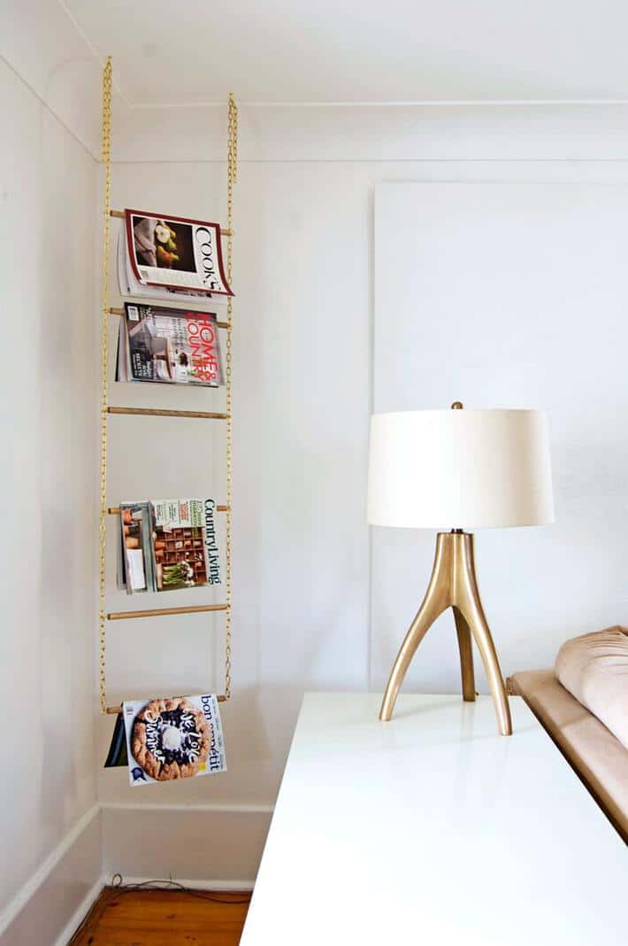 DIY magazine rack made of 2 gold chains with small wood dowels hanging in corner from ceiling.