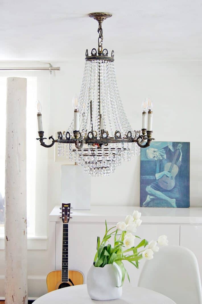 Antique crystal empire style chandelier hangs in an all white modern room.