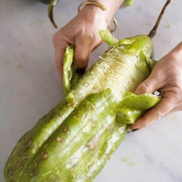 Peeling the skin of a green luffa.