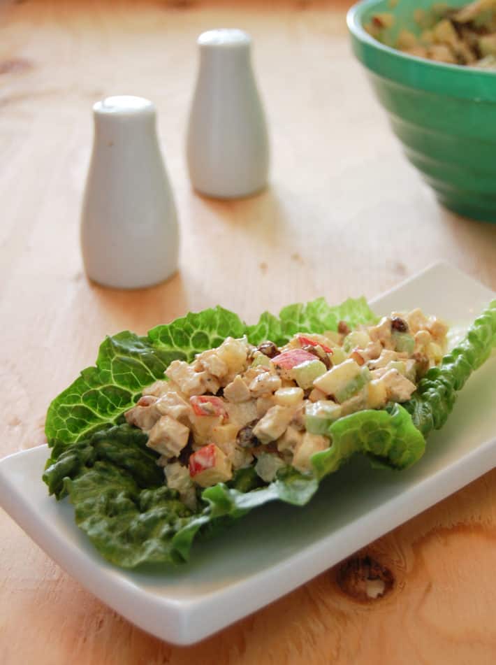 Curry chicken salad with apples and pecans served on a romaine lettuce leaf on a small white rectangular plate.