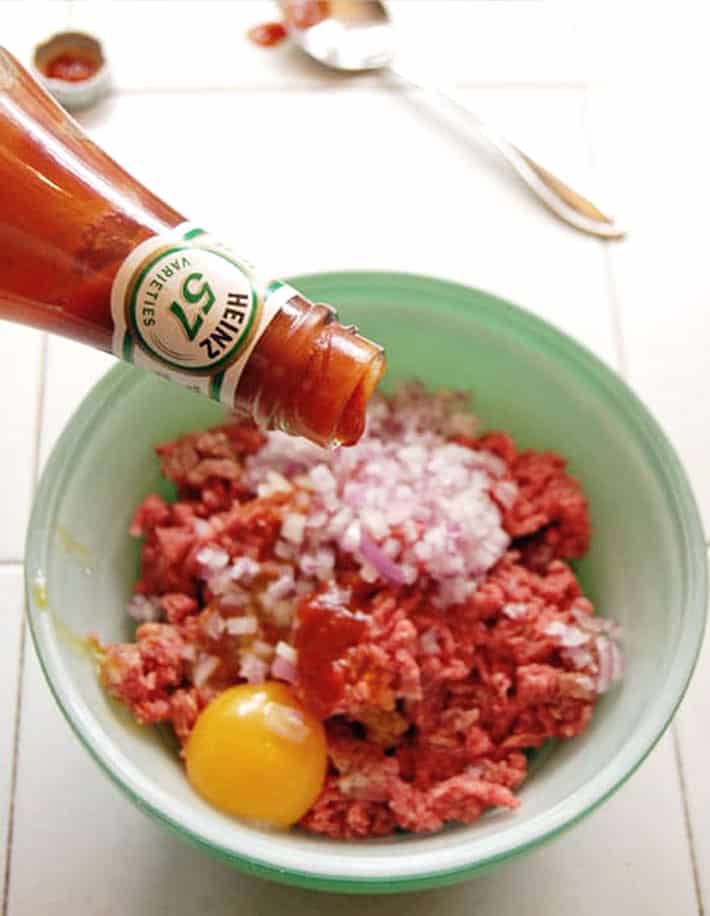 Heinz ketchup dripping into bowl with ground beef, egg and diced onions.