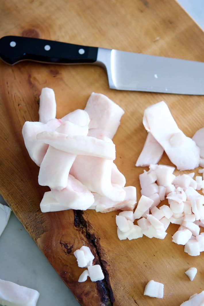 Pork fat being diced on a wood cutting board.