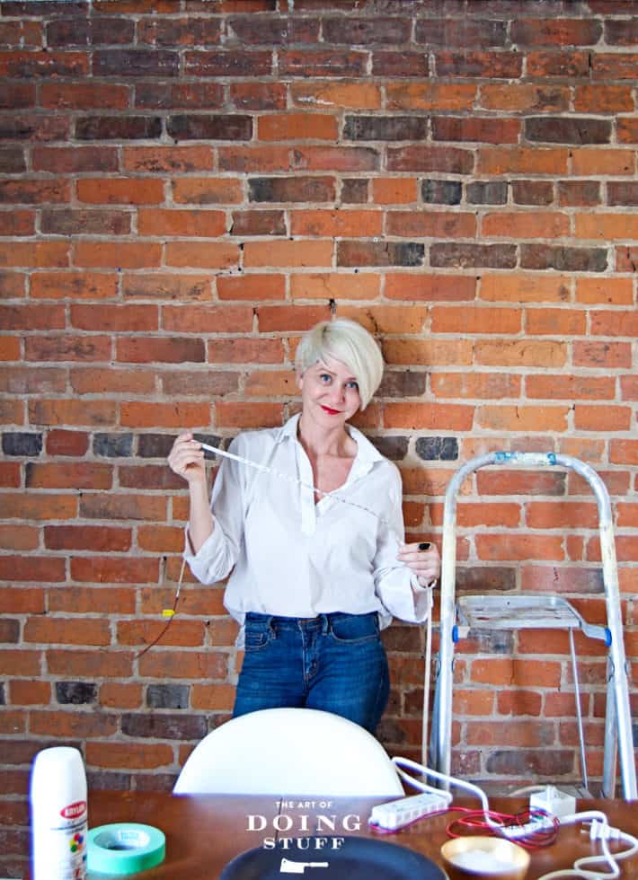 Karen Bertelsen installing LED strip lights on antique brick wall.