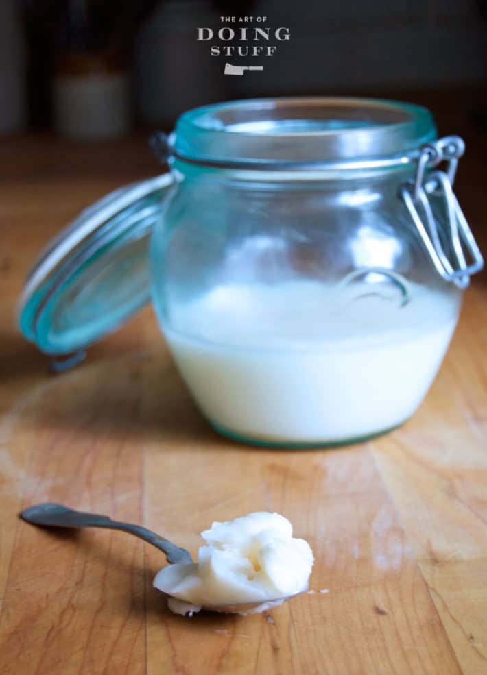 Snow white homemade lard on a spoon with a half full glass jar of lard behind it.