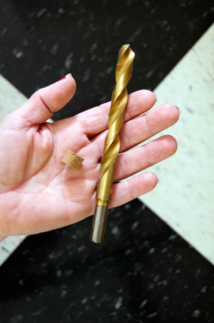 Drill bit and small cork in woman's hand, held over black and white tile floor.