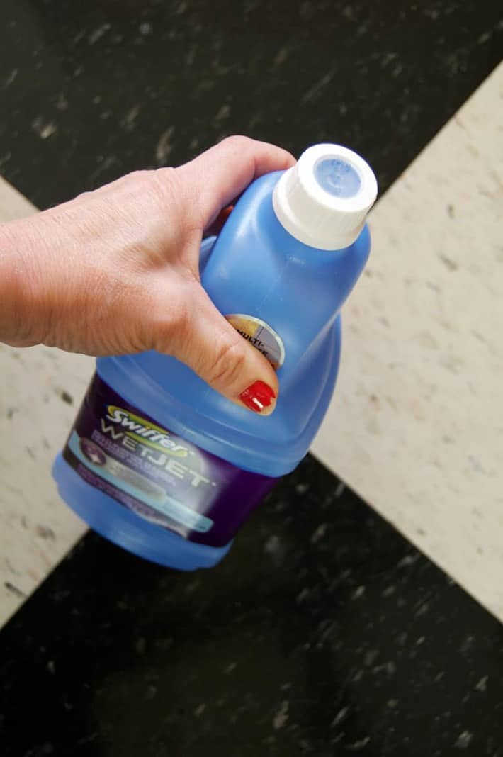 A woman's hand holding a swiffer Wet Jet bottle, showcasing the cap that can't be removed.