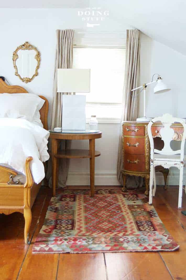 A bedroom with wide plank floors, a Turkish rug, an ornate antique bed covered in fresh white linens.