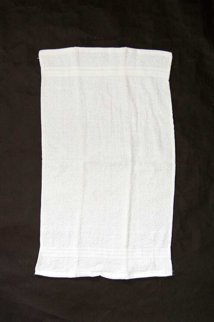 Inexpensive white terrycloth hand towel laid on a black table.