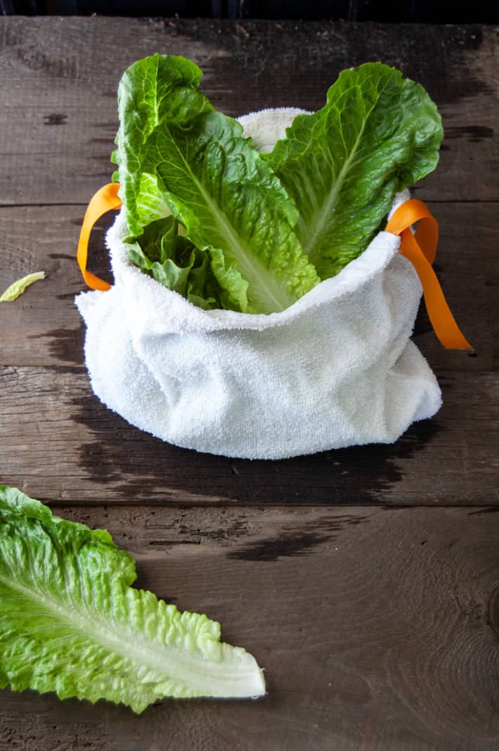 Bright green romaine lettuce sticking out of a white terry towel salad bag on a wood table.