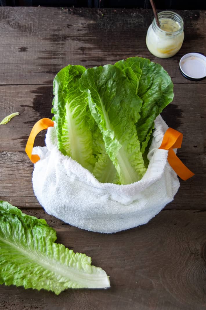 Bright green romaine lettuce in a white terrycloth salad bag sitting on a worn wood table.
