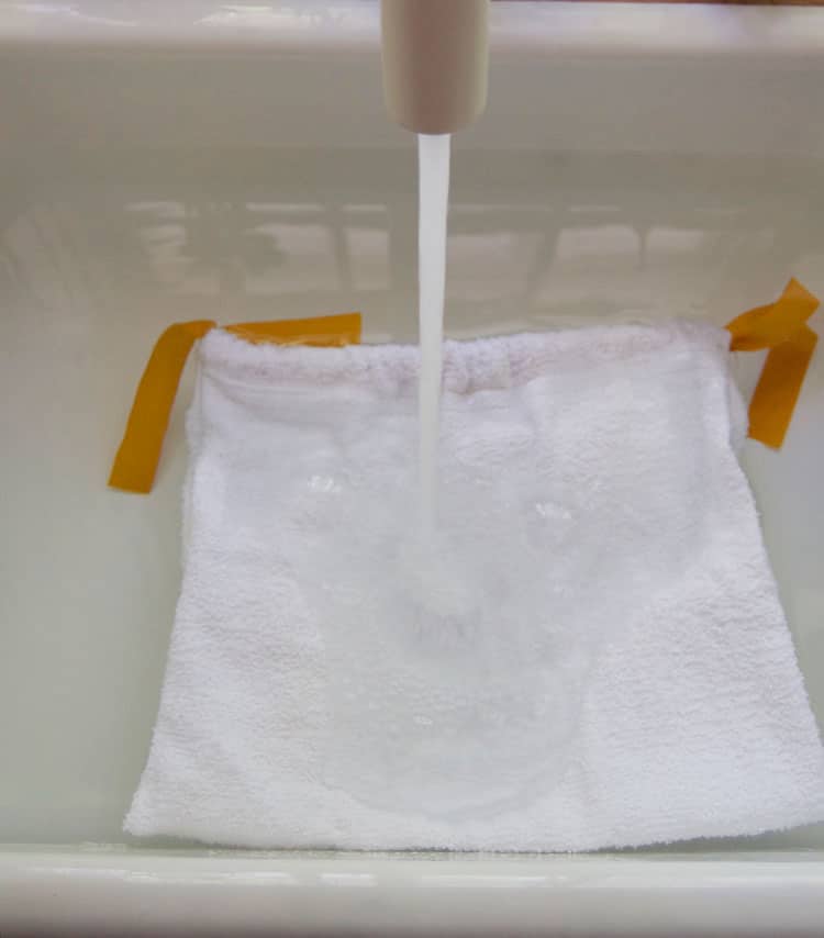 Salad bag being soaked in water in white sink.