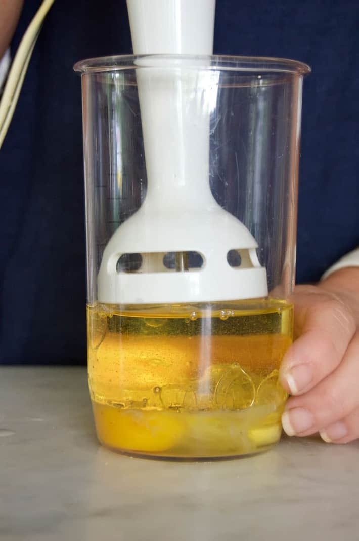 Immersion blender hovering over egg in bottom of jar.