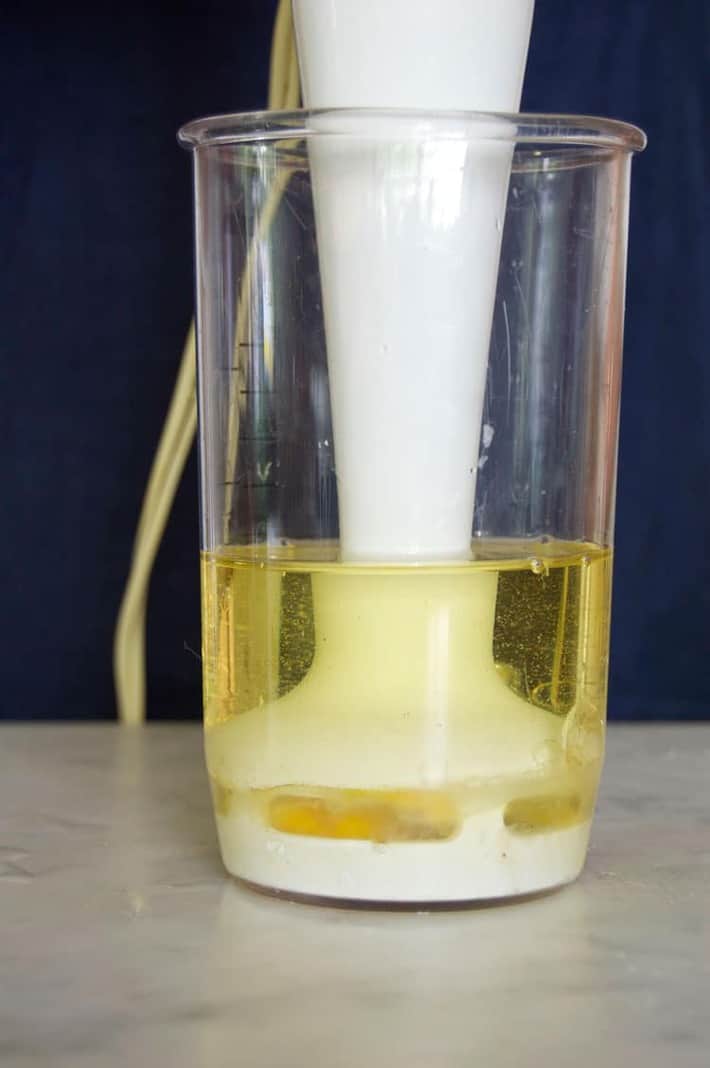 Immersion blender sitting right over a whole raw egg in clear glass container.