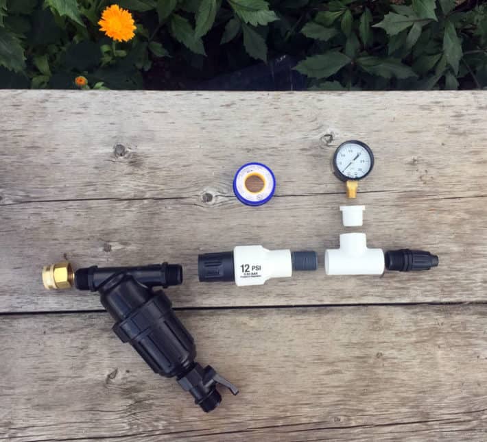 Irrigation filter and pressure reducer laid out on a wood bench in order of how you put them together.