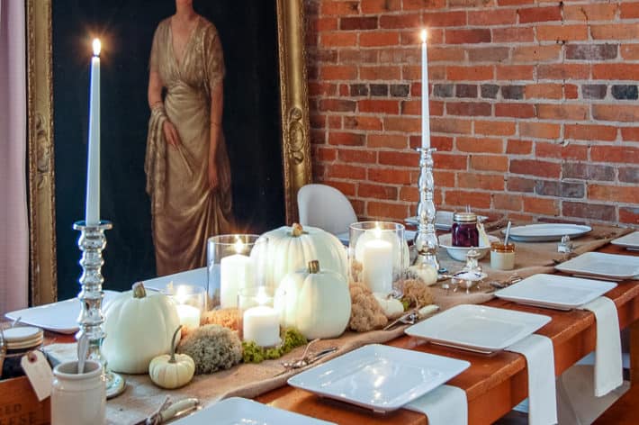 Table set with a table scape of mercury glass candlesticks, white pumpkins, and preserved moss.