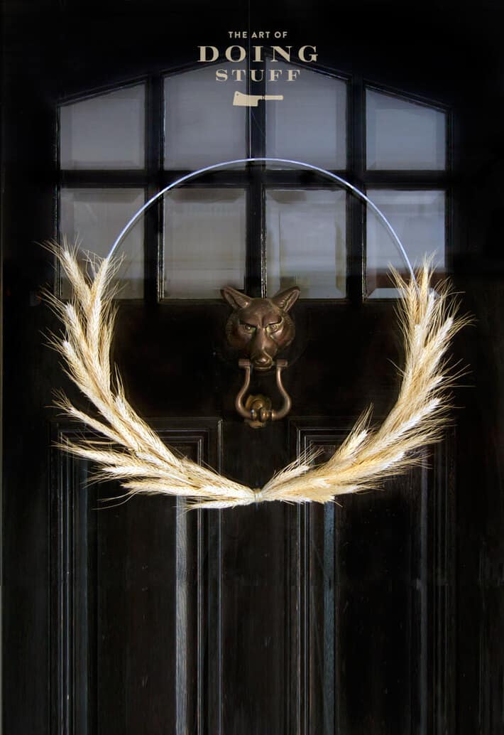 Minimalist fall wheat wreath hangs on a black door with brass fox doorknocker.