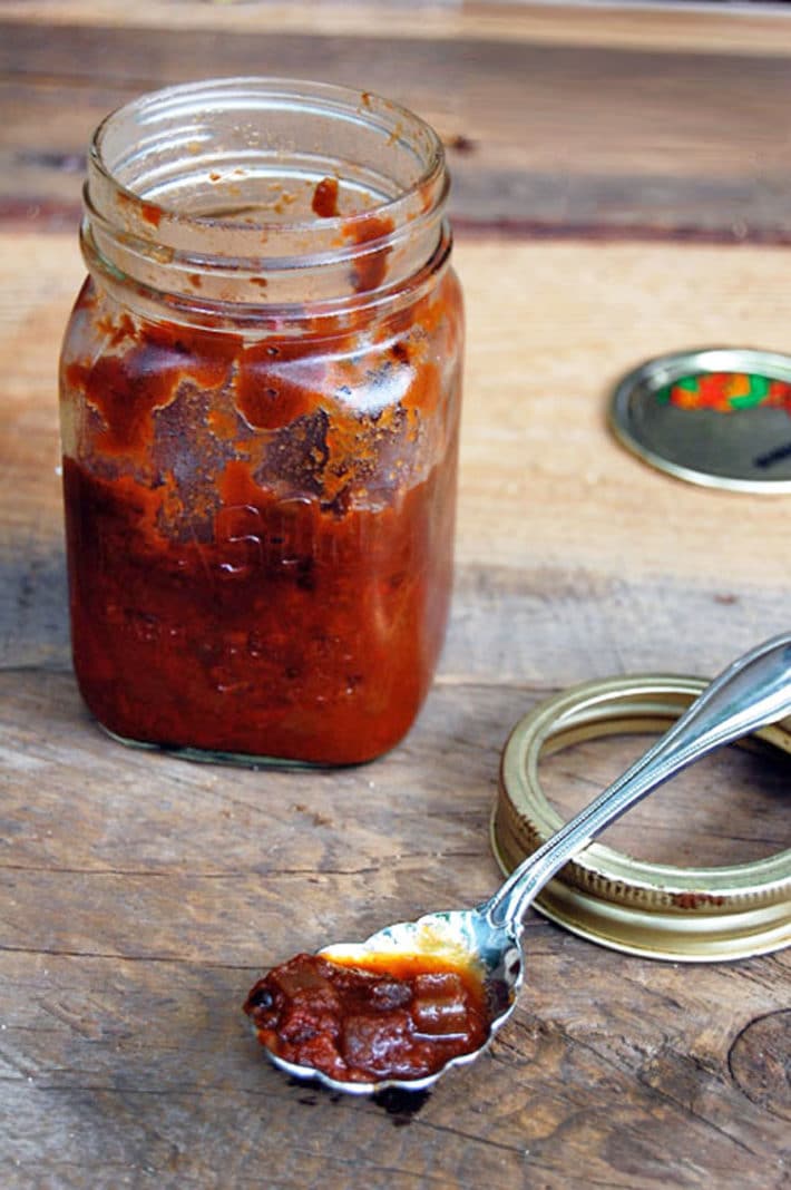 Homemade chili sauce in a vintage square mason jar, set on a barnboard table.