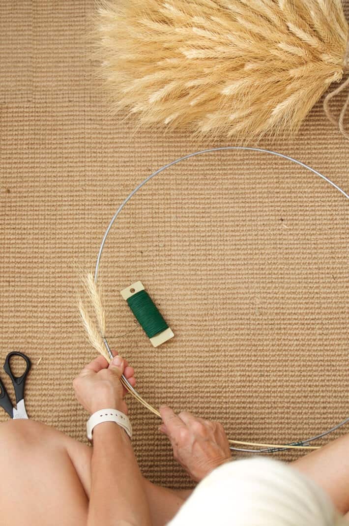 A woman's hands hold wheat onto a round wreath form.