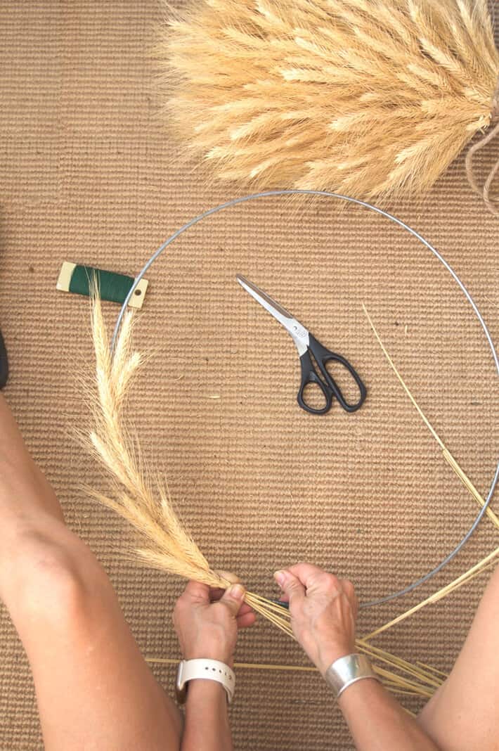Winding thin florists wire around wheat on a wheat wreath on a sisal rug.