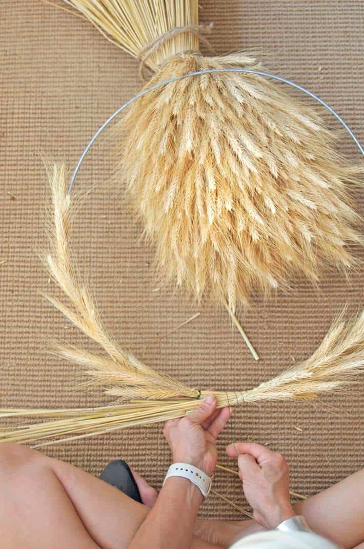 Finishing wrapping wire around wheat in bunches around a wire frame to make a wheat wreath.