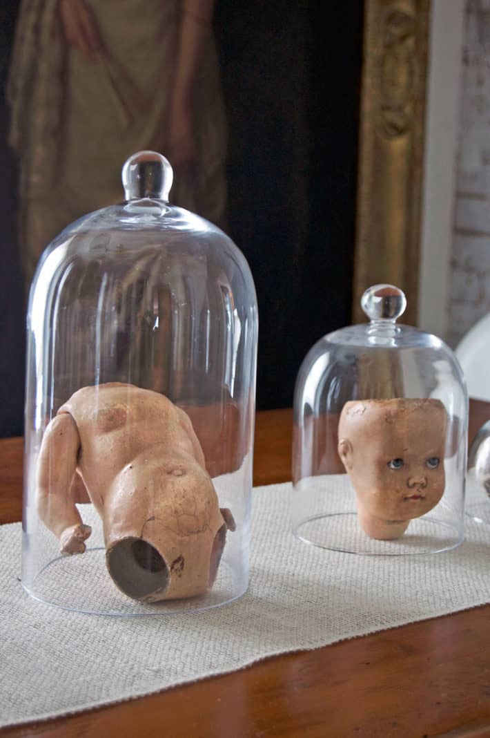 Seriously creepy Halloween decoration of an antique doll torso under a glass cloche on dining room table.